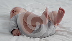 Childbirth Concept. Closeup Of Chubby Newborn Baby Wearing Bodysuit Lying On Bed