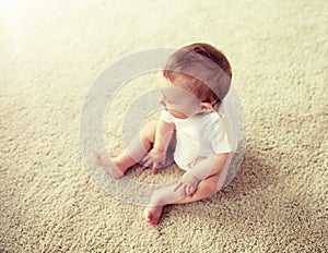 Happy baby boy or girl sitting on floor at home