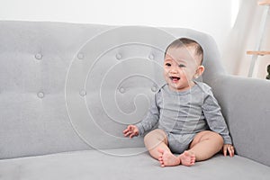 Childhood, babyhood and people concept - happy little baby girl sitting on sofa at home