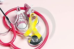 Childhood Cancer Awareness Golden Ribbon with baby sneakers and stethoscope on pink background
