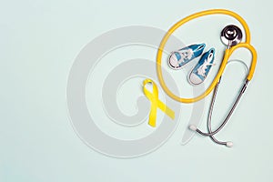 Childhood Cancer Awareness Golden Ribbon with blue baby sneakers and stethoscope on blue background with copy space. C