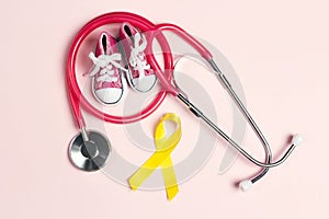 Childhood Cancer Awareness Golden Ribbon with blue baby sneakers and stethoscope on pink background with copy space