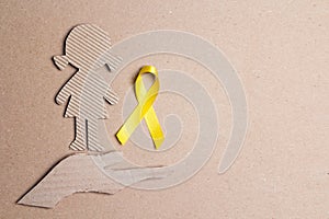 Childhood Cancer Awareness Golden Ribbon with girl cardboard doll and hand silhouette on cardboard background