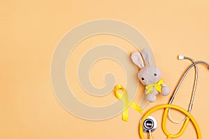 Childhood Cancer Awareness Yellow Ribbon with toy bunny and stethoscope on yellow background with copy space