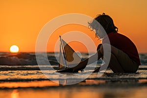 Childhood concept. Kid boy holding tou boat. Cute little blond boy put toy boat in the sea. Dream on travel. Sea dream