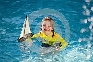 Childhood concept. Kid boy holding tou boat. Cute little blond boy put toy boat in the sea water waves at the beach on