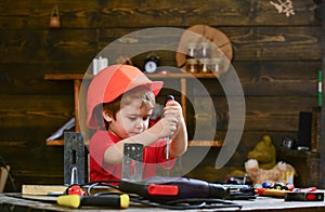 Childhood concept. Kid boy in orange hard hat or helmet, study room background. Boy play as builder or repairer, work