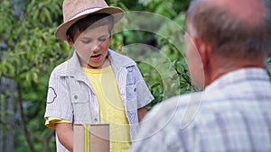 childhood, cute male child helping his grandfather beekeeper paints hives with paint while relaxing in countryside