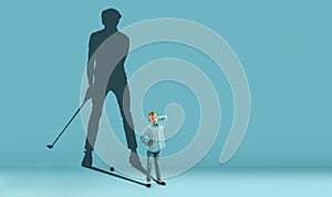 Childhood and dream about big and famous future. Conceptual image with boy and shadow of fit male golf player on blue