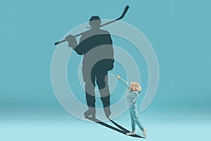 Childhood and dream about big and famous future. Conceptual image with boy and shadow of fit male hockey player on blue