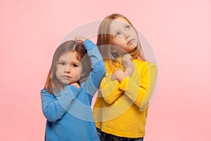 Childhood dreams. Portrait of two pensive beautiful little girls scratching head or looking up with thoughtful expression