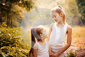 Childhood, family, friendship and people concept - two happy kids sisters hugging outdoors.