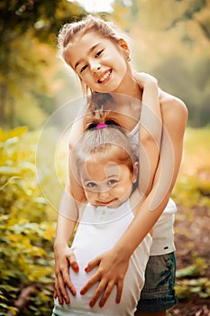 Childhood, family, friendship and people concept - two happy kids sisters hugging outdoors.