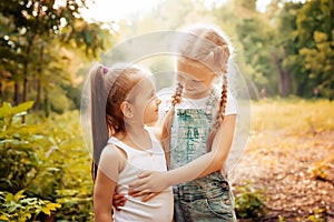 Childhood, family, friendship and people concept - two happy kids sisters hugging outdoors.