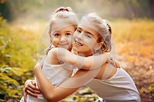 Childhood, family, friendship and people concept - two happy kids sisters hugging outdoors.