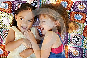 Childhood firendship. High angle shot of two little girls lying down and playing on a blanket.