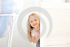 Childhood, fun and people concept - happy smiling beautiful little girl hiding behind room door. The child plays hide and seek at