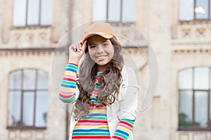 Childhood happiness. Happy girl with curly hair wearing cap. Child smiling outdoors. Beauty and fashion. You would not