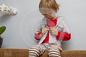 Childhood independence concept ,little boy buttoning on shirt, fastening his buttons , on white gray background. The