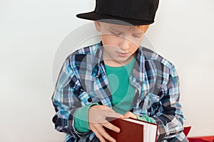 Childhood and leisure. Image of schoolboy in stylish checked shirt and cap opening red book isolated over white background wanting