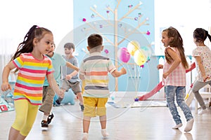 Childhood, leisure and people concept - group of happy kids playing tag game and running in spacious room