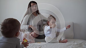 Childhood, motherhood, siblings concept - carefree young mum combs her little kid daughter hair , son and newborn baby