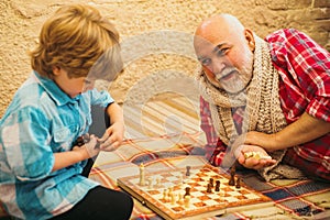 Childhood. Senior man teaching his grandson to play chess. Kid Playing Chess. Grandfather and grandson concept.