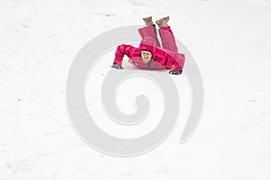 childhood, sledging and season concept - happy little girl sliding down on sled outdoors in winter