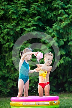 Childhood summer games with water pool. Caucasian brother and sister play with plastic toys watering can pouring water splashing,