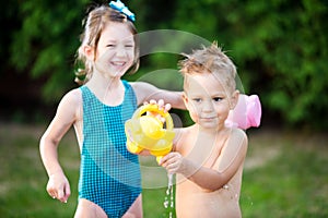 Childhood summer games with water pool. Caucasian brother and sister play with plastic toys watering can pouring water splashing,