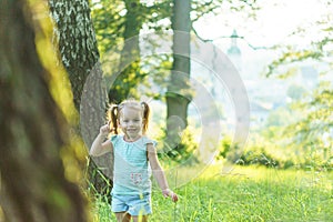 Childhood, summer and leisure concept.One cute happy little baby standing in bright grass with dandelions in backlight