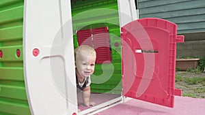 Childhood, toddler, motherhood, summer. Happy smiling Baby Boy Kid playing hide-and-seek and looks out the window in