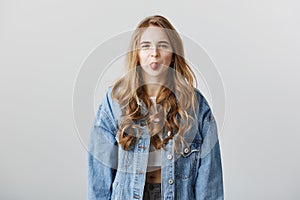 Childish girl do not like you. Indoor shot of impolite attractive woman in denim jacket showing tongue, expressing