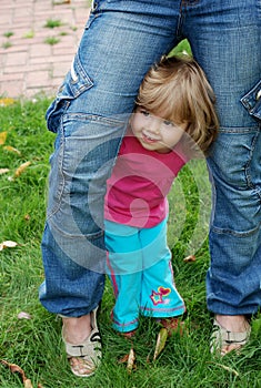 Childish shyness, timidity, insecurity. A defenseless child seeks support from a parent. Cute little girl hiding behind