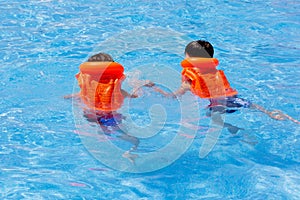 Children, 2 boys in rescue jacket swim in the water. Pool