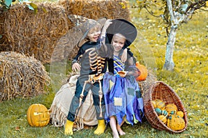 Children in America celebrate Halloween. Happy Halloween Children girl and boy sit on hay or straw on meadow in autumn.