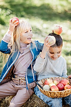 Children with Apple in Orchard. Harvest Concept. Garden, mixed race boy and blonde girl eating fruits at fall