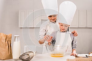 children in aprons and chef hats whisking eggs in bowl at table