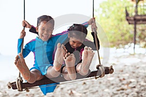 Children bare feet with sand while they playing on a swings together at the beach near the sea in vacation