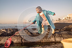 Children, beach and fishing with a girl using a net in a rock pool while having fun on summer vacation. Water, nature