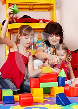 Children with block and woman in play room.