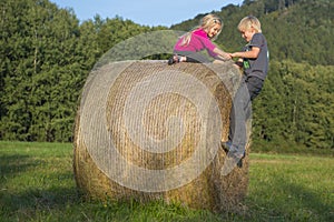 Children blond girl and boy (siblings) resting on hay bale, summer, holiday, relaxing, playing