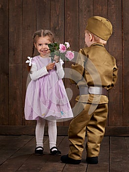 Children boy are dressed as soldier in retro military uniforms and girl in pink dress