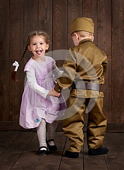 Children boy are dressed as soldier in retro military uniforms and girl in pink dress