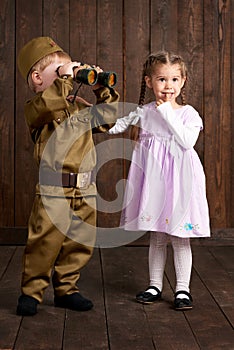 Children boy are dressed as soldier in retro military uniforms and girl in pink dress