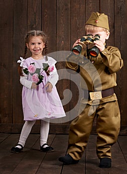 Children boy are dressed as soldier in retro military uniforms and girl in pink dress