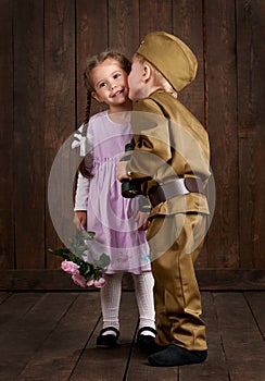 Children boy are dressed as soldier in retro military uniforms and girl in pink dress