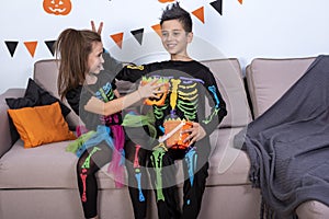 Children boy frightens girl sitting on the sofa preparing for Halloween party decoration.