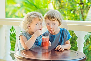 Children boy and girl drink orange smoothie from papaya