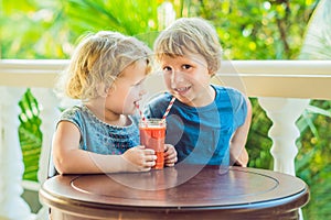 Children boy and girl drink orange smoothie from papaya